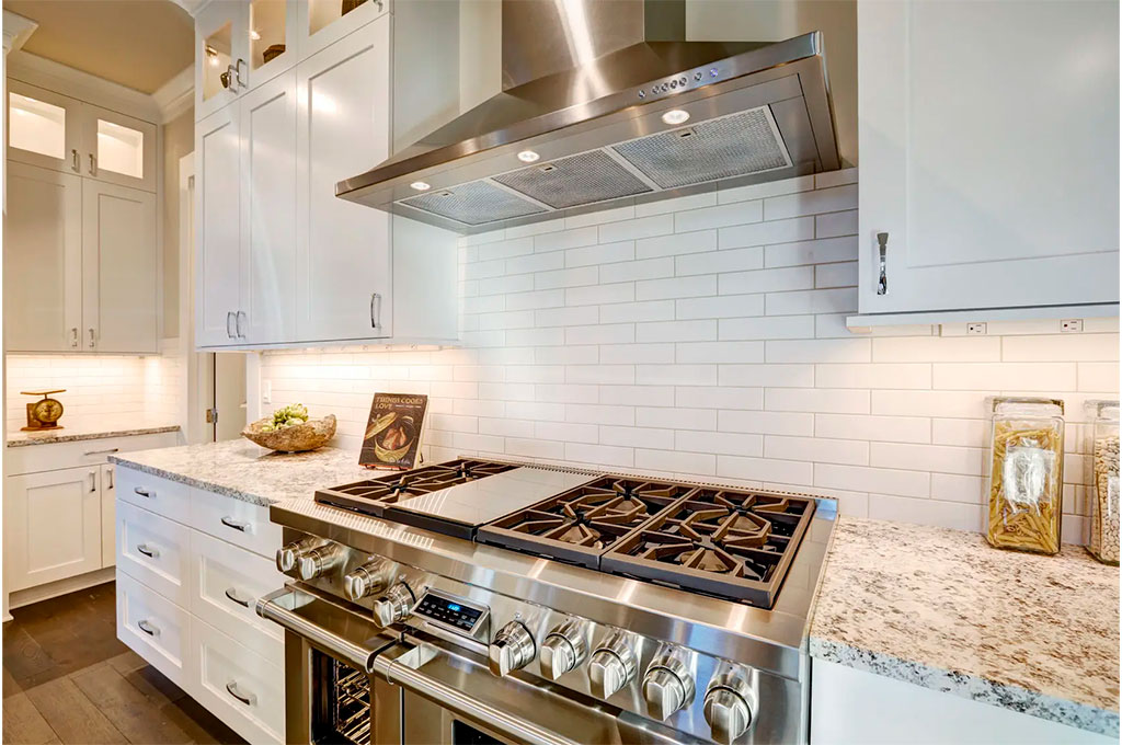 A high-end stove with white tile backsplash & stainless steel range hood.