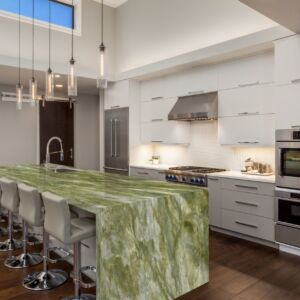 A modern white kitchen with a green and white marble waterfall island.